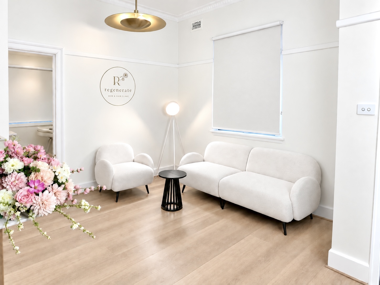 The clinic waiting room, with a full sofa and armchair, the Regenerate wall logo and a floral display